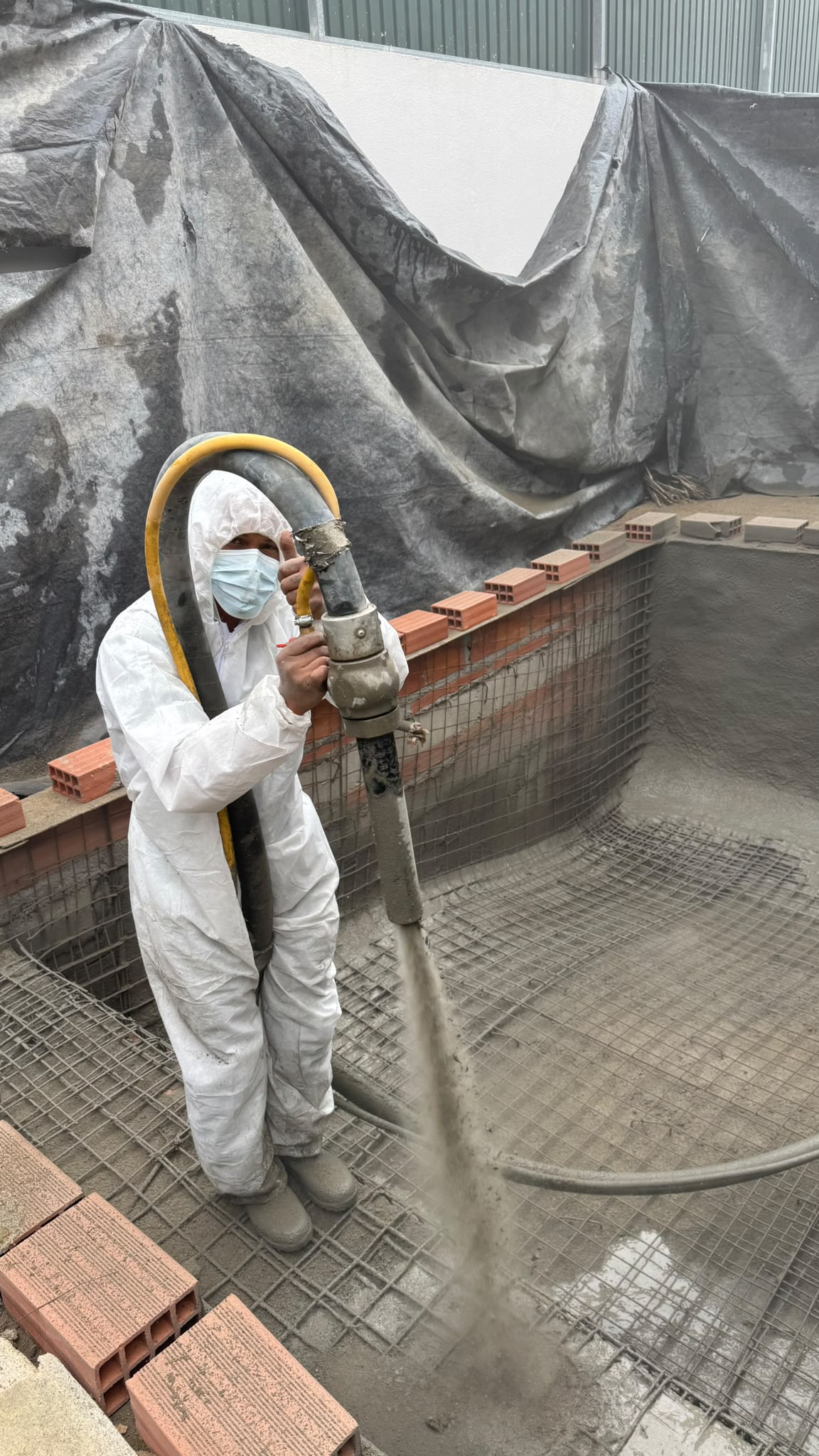 Operador a aplicar betão projetado com equipamento de proteção
